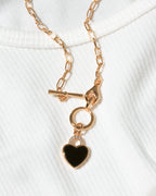 Gold toggle clasp chain necklace with black onyx heart pendant on a white ribbed knit top