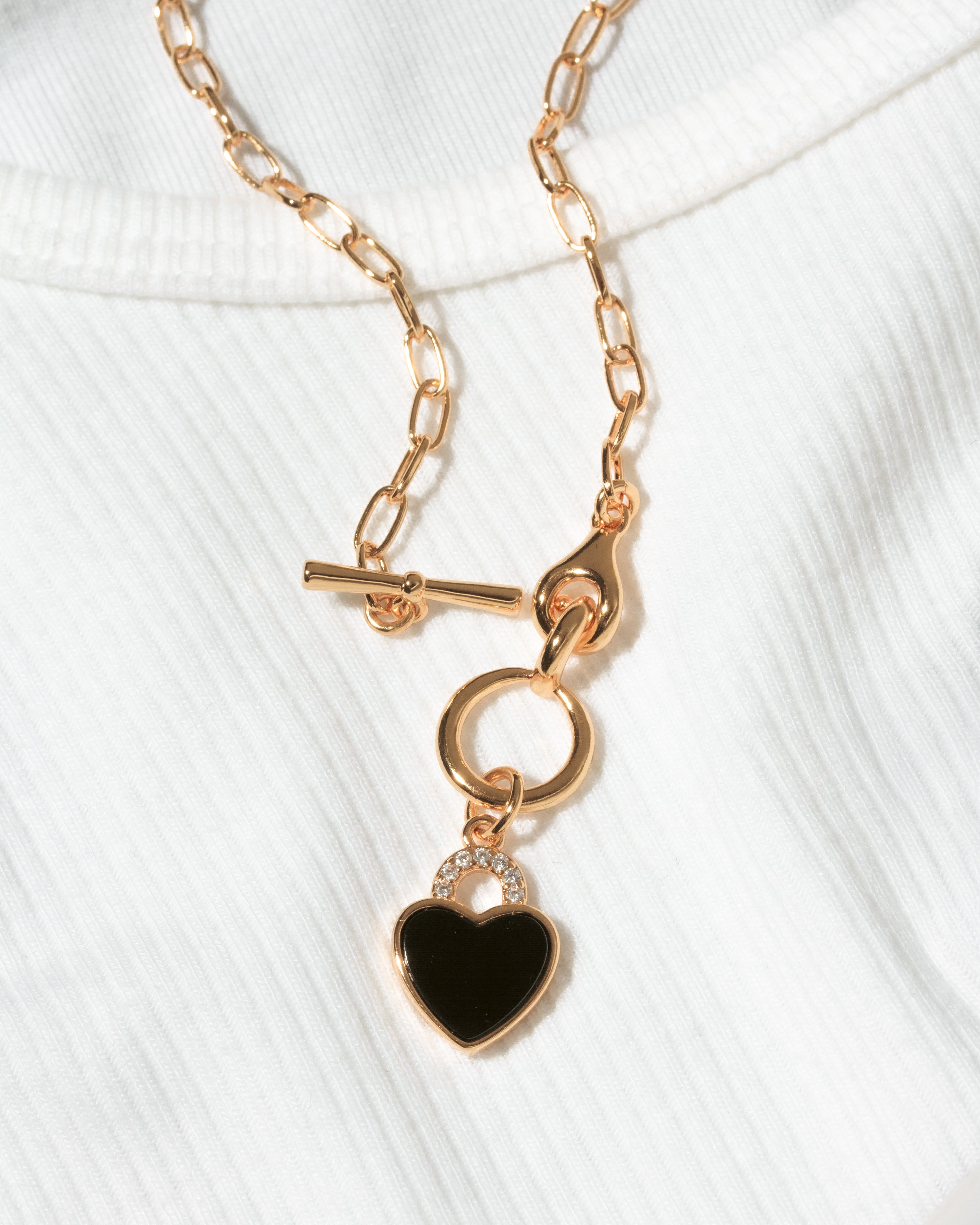 Gold toggle clasp chain necklace with black onyx heart pendant on a white ribbed knit top