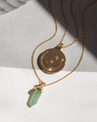 Gold necklace with a green pendant on a light gray background