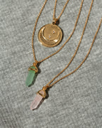Three gold necklaces: one with a crescent moon and star coin, and two with gemstone prism charms.
