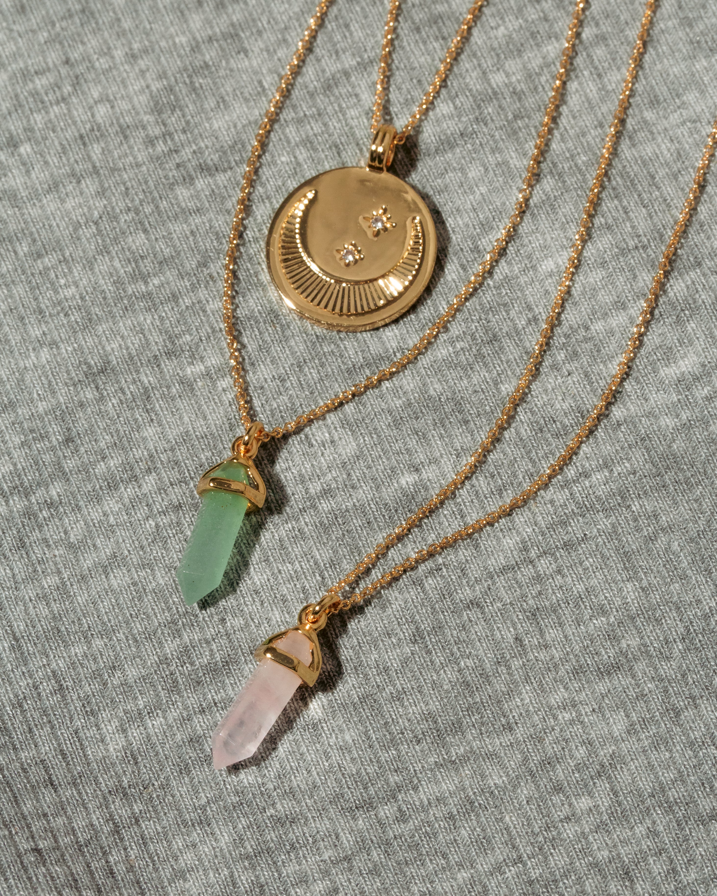 Three gold necklaces: one with a crescent moon and star coin, and two with gemstone prism charms.
