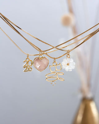 Three gold necklaces with charms on a light gray background