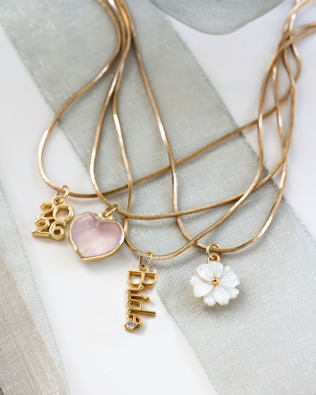 The necklaces include charms: a pink heart, a gold 2026 charm, a white flower charm, and a gold vertical charm with the word 'Bride'.