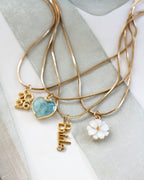 The necklaces include charms: a gold 2026 script pendant, a light blue heart-shaped stone pendant, a white flower charm, and a gold Bride lettering charm.