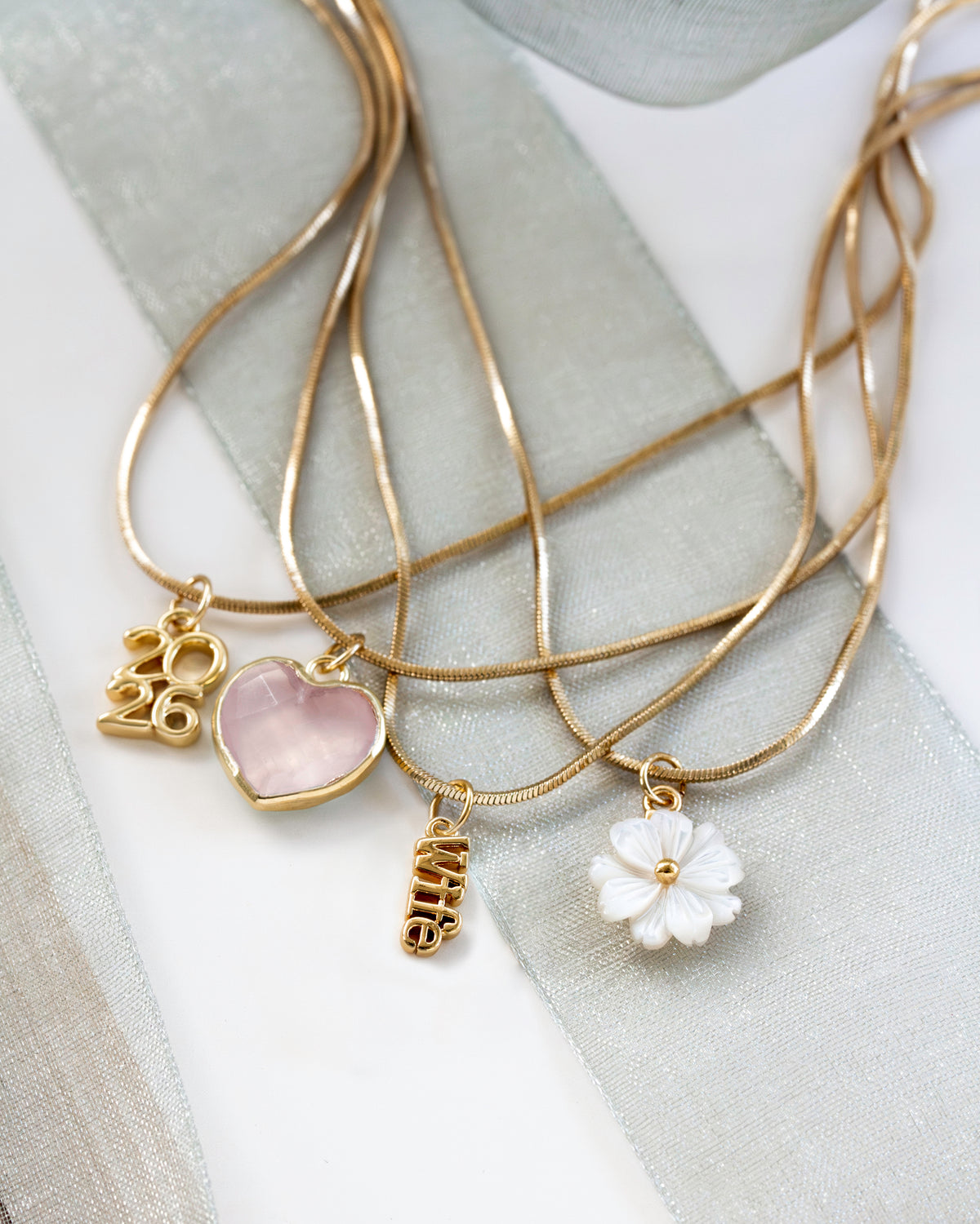 Gold layered charm necklace with 4 charms a rose quartz heart, a 'WIFE' charm, year 2026 charm and a mother of pearl flower.