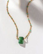 Gold chain necklace featuring an emerald pendant and aquamarine-colored beads.