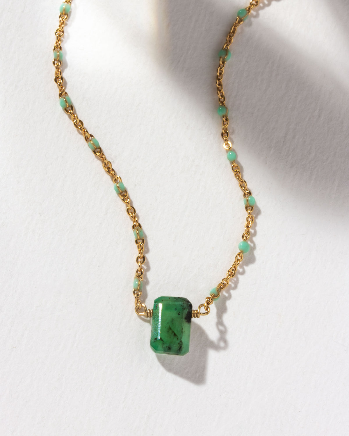 Gold chain necklace featuring an emerald pendant and aquamarine-colored beads.