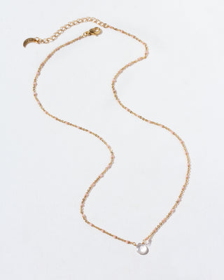 Gold necklace with a clear teardrop gemstone pendant on a light gray background