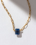 Gold chain necklace with a sapphire gemstone.