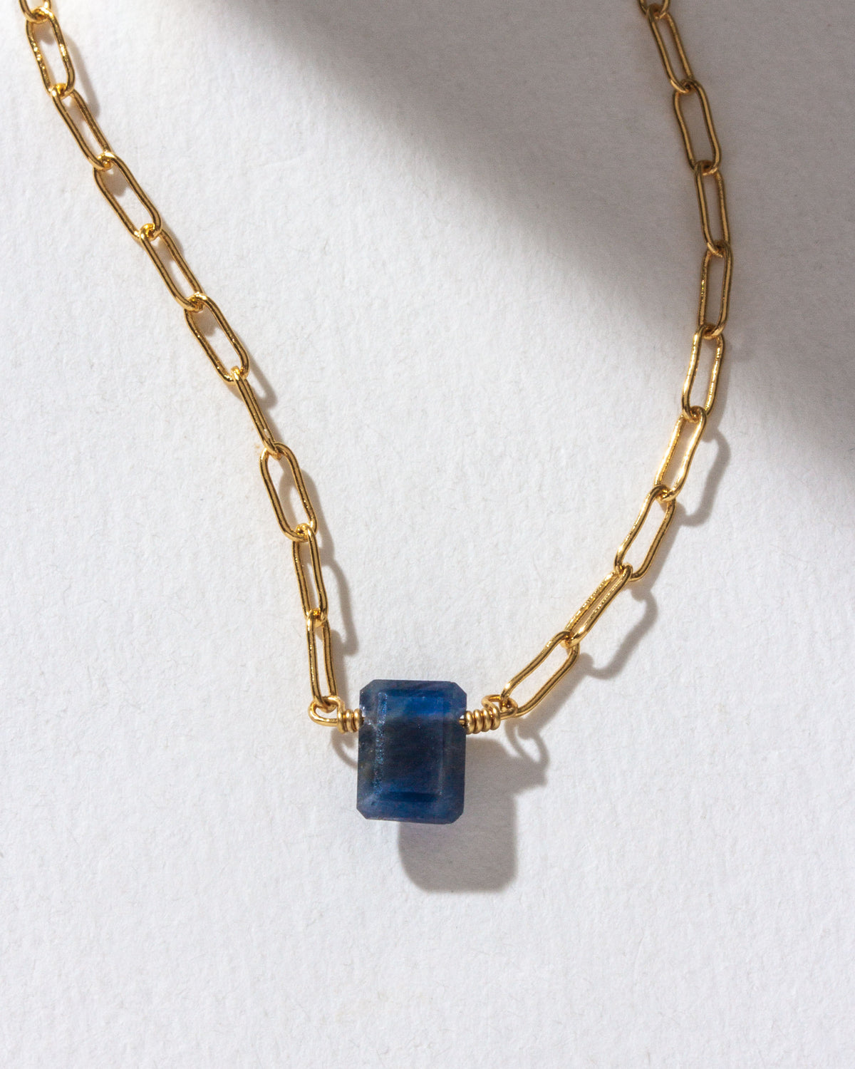Gold chain necklace with a sapphire gemstone.