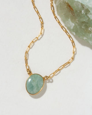 Gold chain necklace with a green aquamarine gemstone pendant on a light background