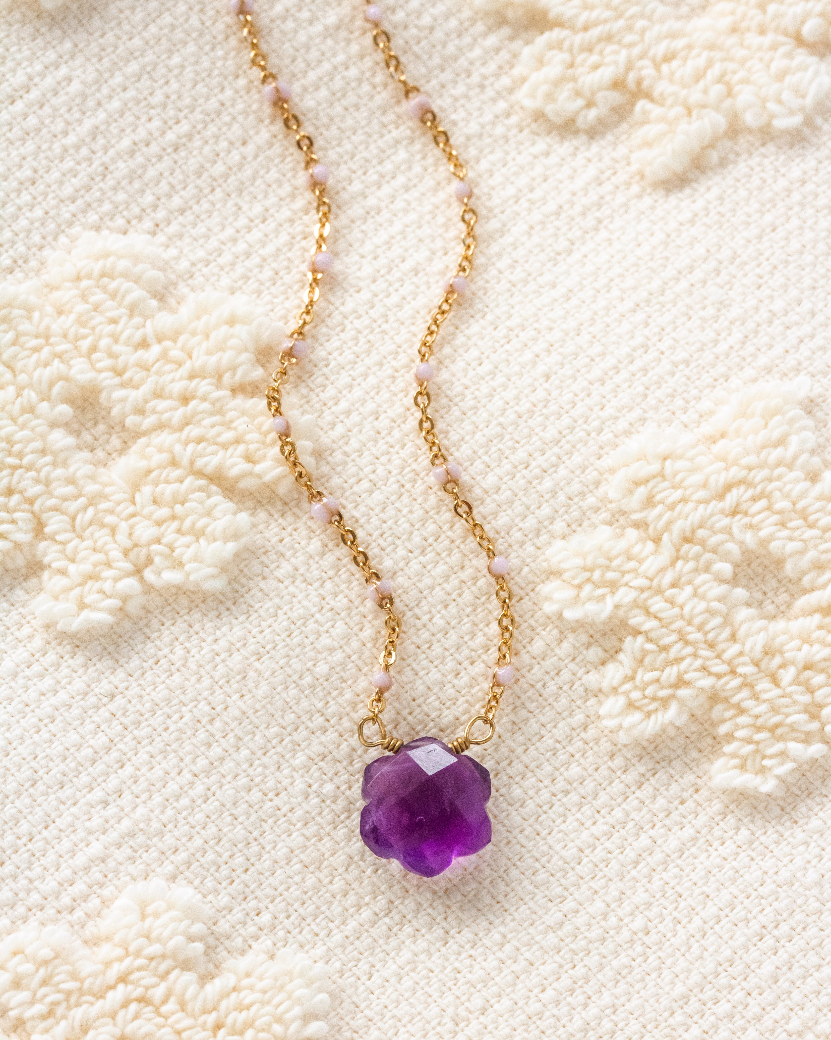 Gold necklace with a purple flower-shaped pendant on a textured white background