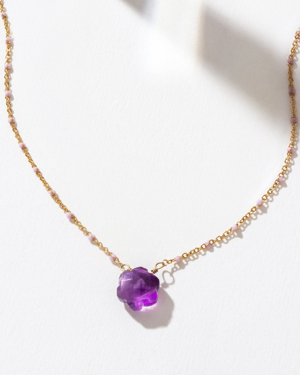 Gold necklace with floral shaped amethyst gemstone pendant on a white background