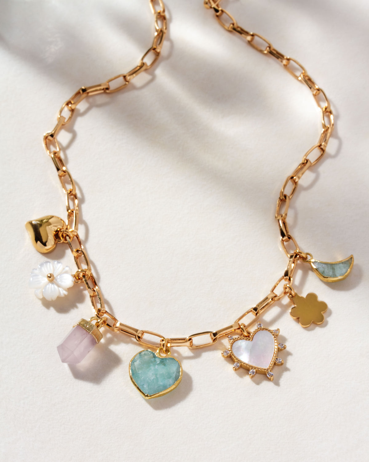 Gold charm necklace with mother-of-pearl, rose quartz, and aquamarine charms, with hearts and flower