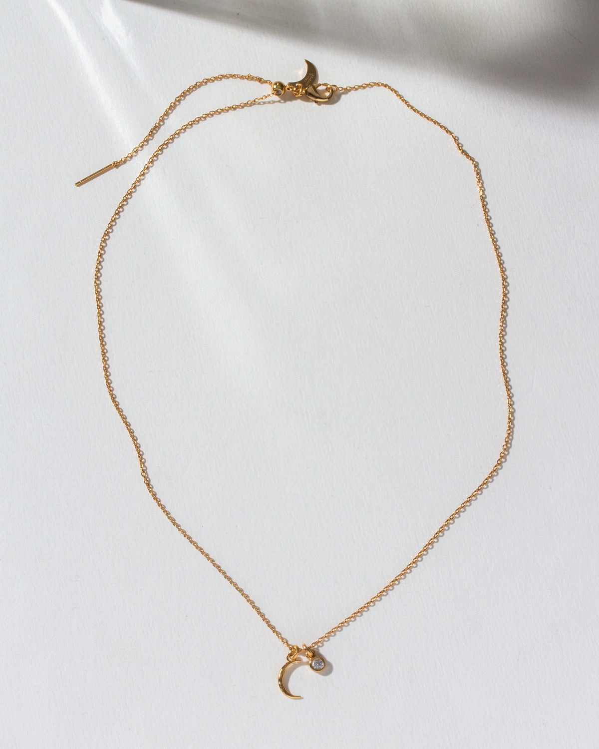 Gold necklace featuring a hammered crescent moon and small CZ charm.