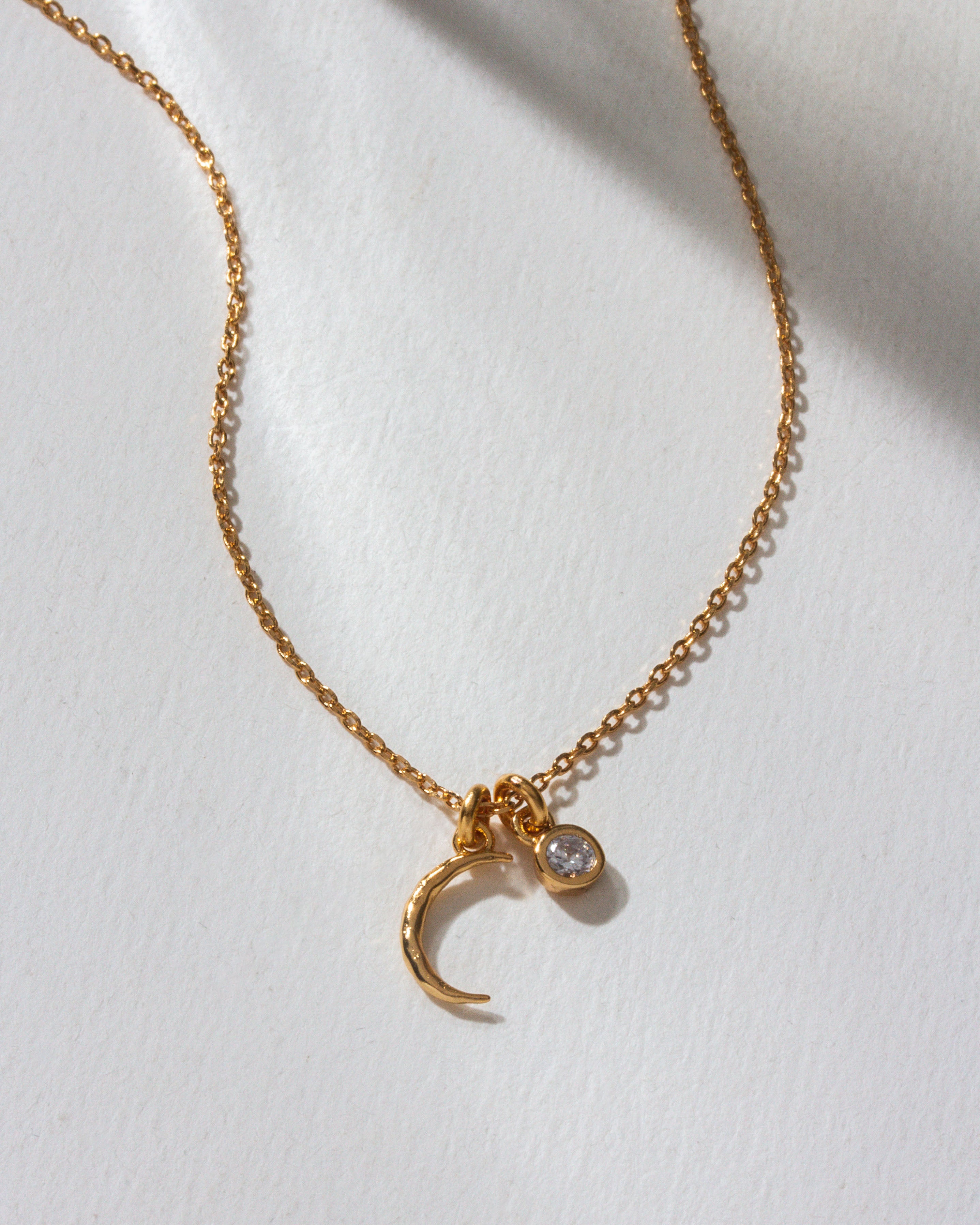 A gold chain necklace with a crescent moon and small clear gem charm.