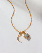 A gold-colored necklace with a crescent moon and star charm on a white surface.