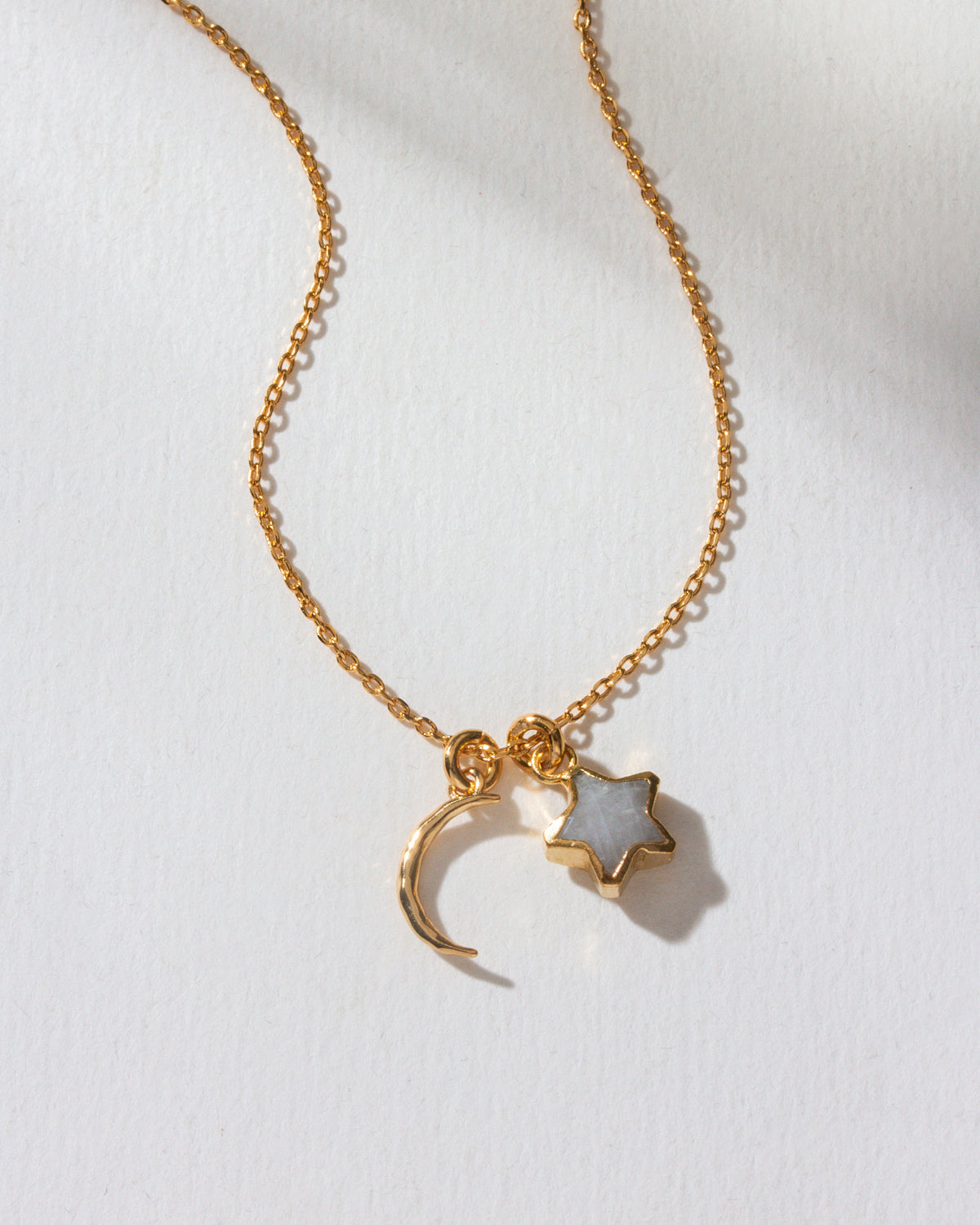 A gold-colored necklace with a crescent moon and star charm on a white surface.