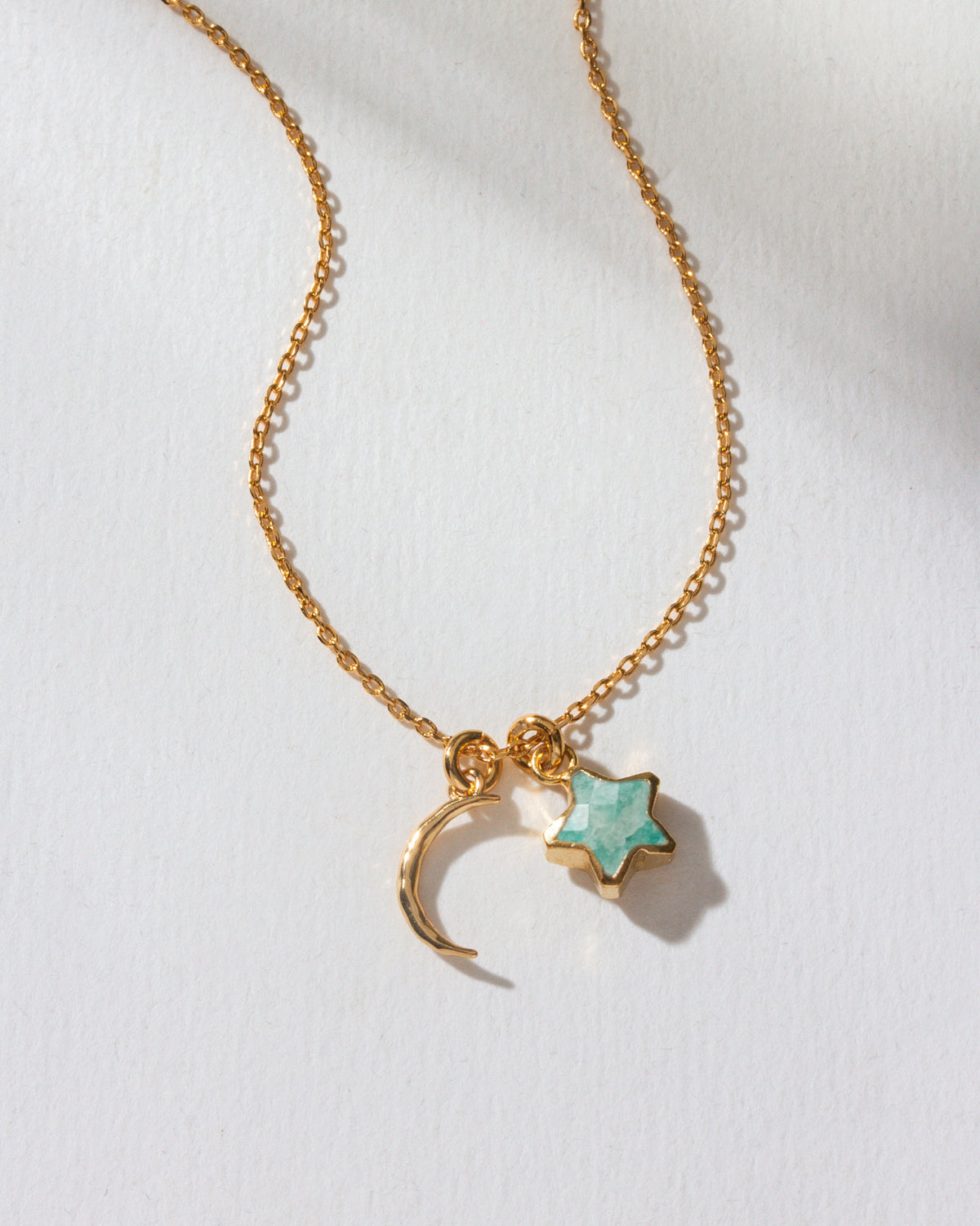 A gold-colored necklace with a crescent moon and amazonite star charm.