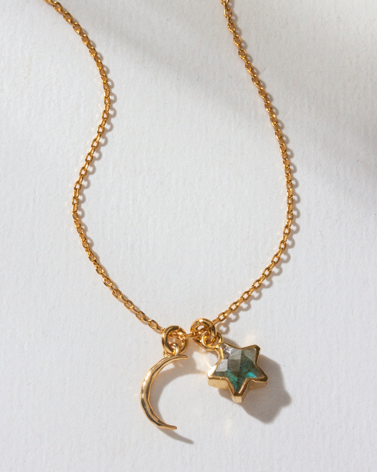 A gold necklace with a hammered crescent charm and a labradorite gem star charm