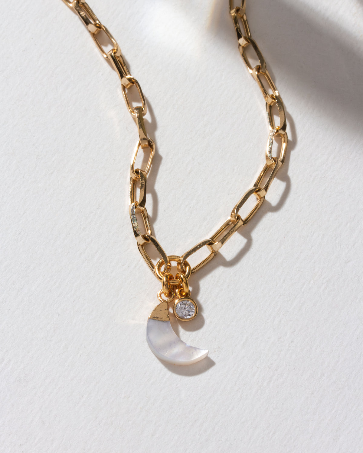 Gold paperclip chain necklace with a mother-of-pearl crescent charm and CZ stone.