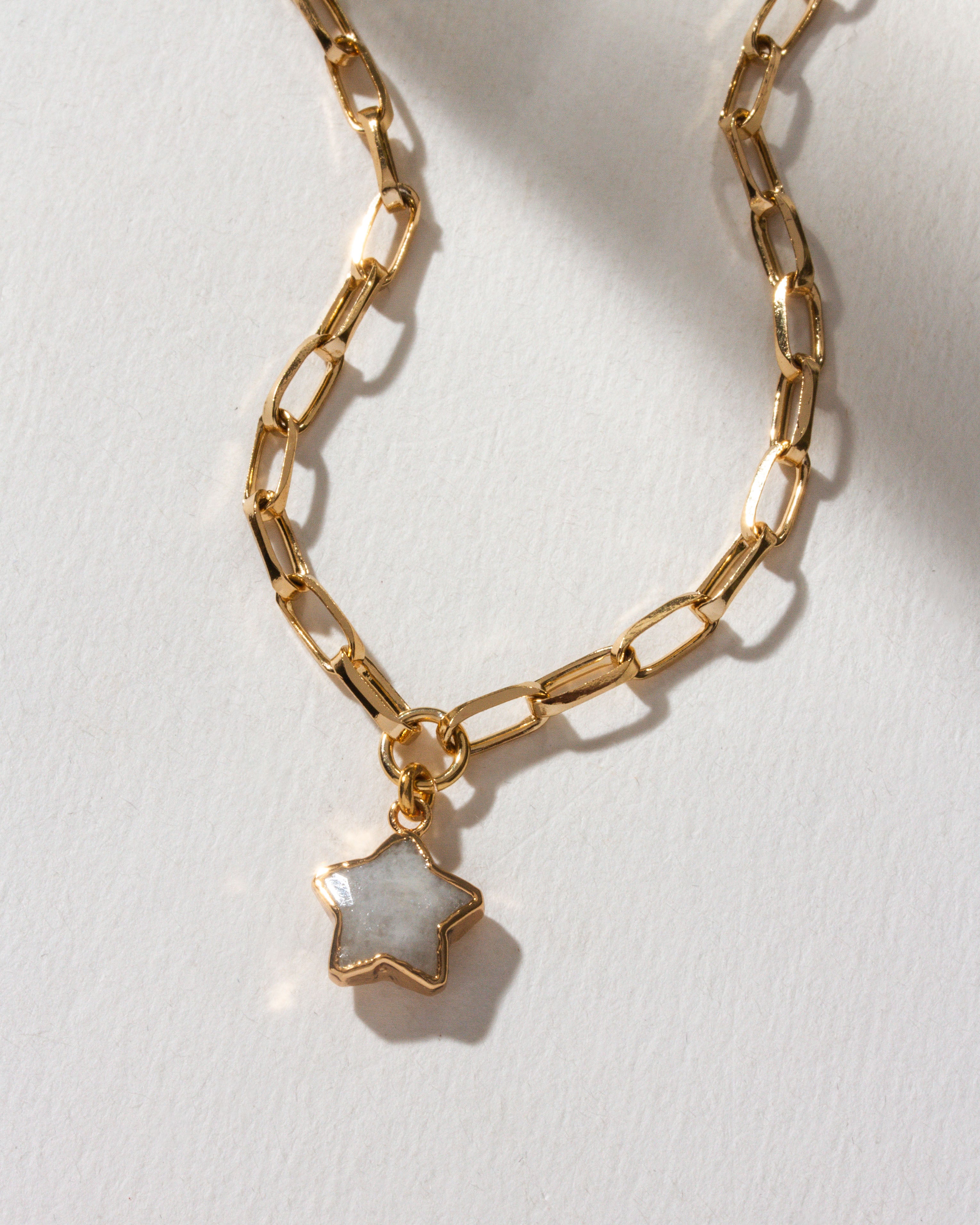Gold paperclip chain necklace with a moonstone star pendant on a white background.