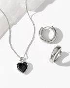 Silver jewelry set featuring a heart-shaped pendant necklace with a black onyx heart inlay, and matching silver huggie hoop earring.