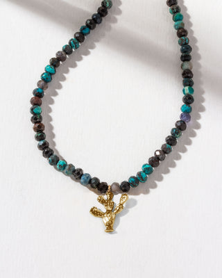 Necklace with black and blue Chrysocolla beads and a golden prickly pear cactus charm on a white background