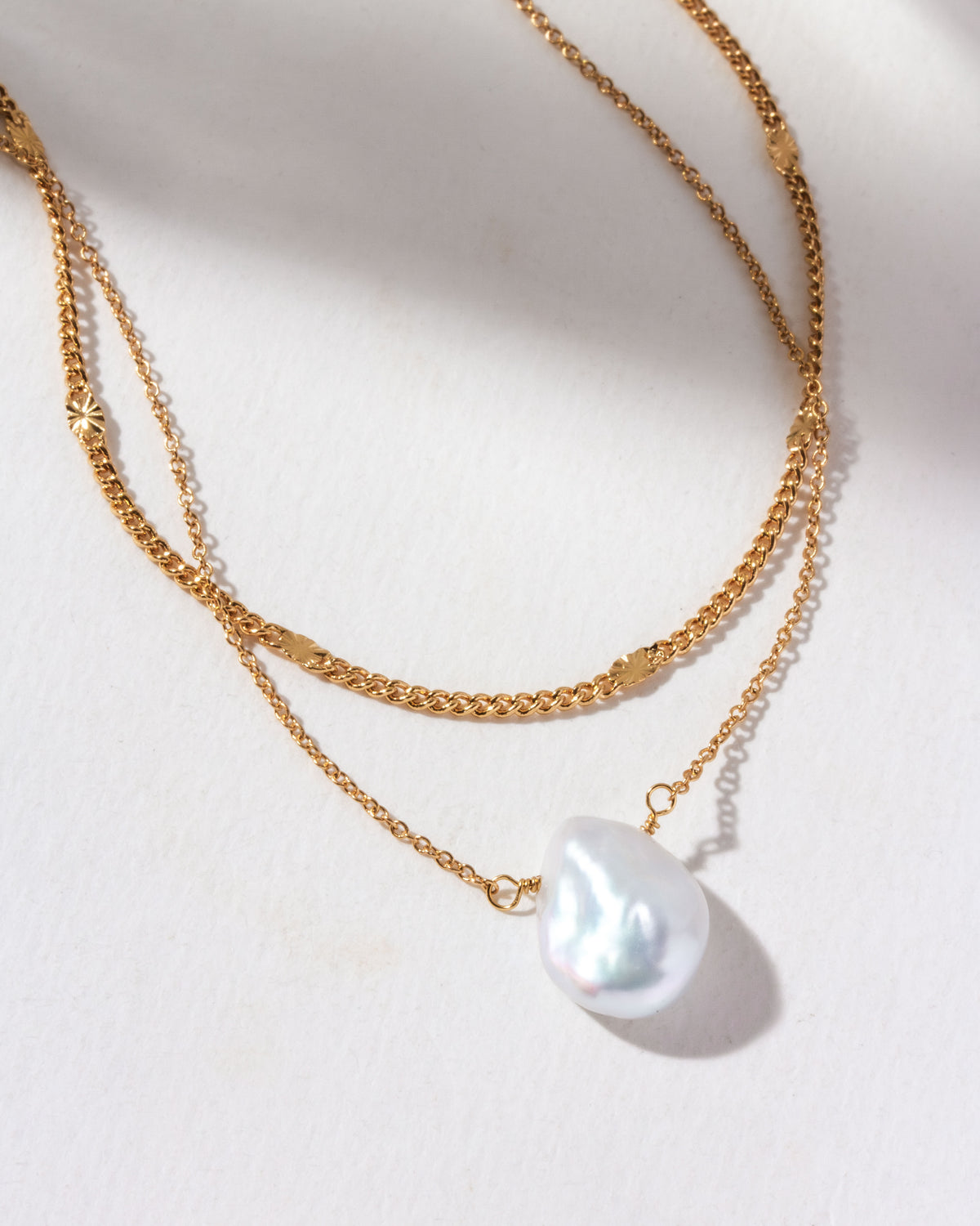 Gold layered necklace with curb and oval link chains, featuring a baroque pearl.