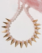 A beaded necklace with pale pink rose quartz translucent beads and metallic gold spikes.
