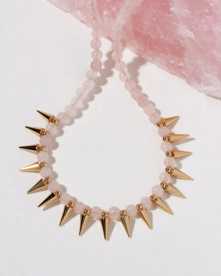 A beaded necklace with pale pink rose quartz translucent beads and metallic gold spikes.