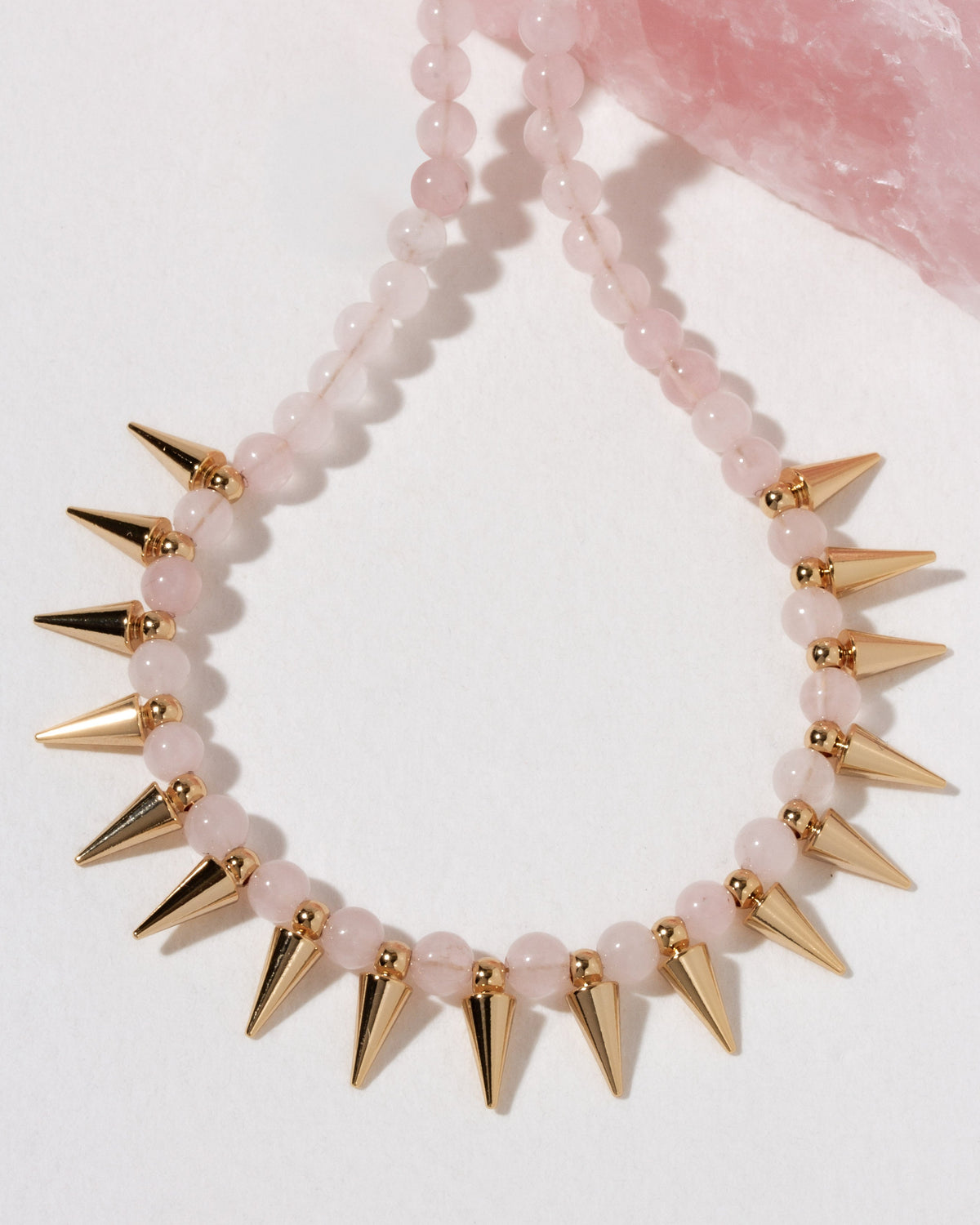 A beaded necklace with pale pink rose quartz translucent beads and metallic gold spikes.