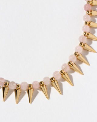 A close-up of a necklace featuring light pink round beads and gold-tone spiked beads.