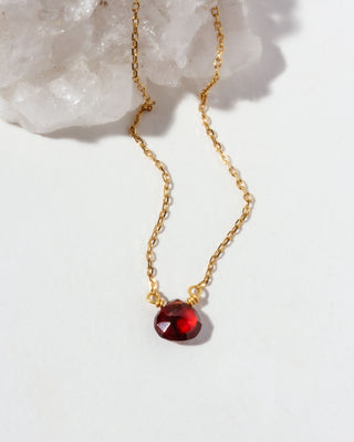 Gold chain necklace with a red garnet gemstone pendant on a white background