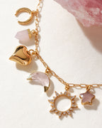 Gold charm necklace with moon, heart, crystal point, crescent moon, sunburst, and star charms.