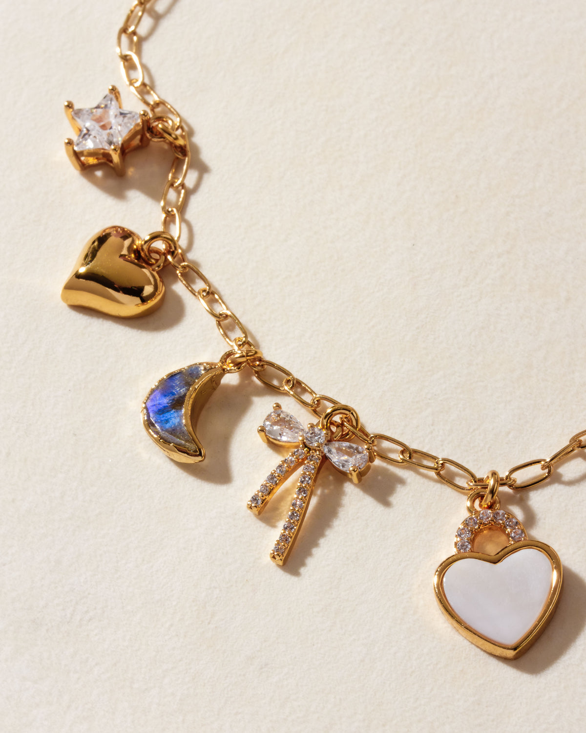 Gold charm necklace with mother-of-pearl heart, labradorite moon, bow, and star charms