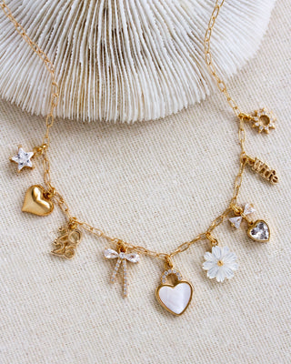 Gold necklace with various charms on a textured beige surface