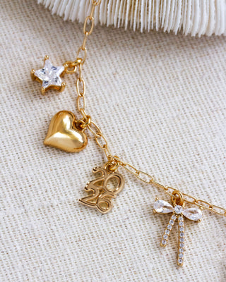 Gold necklace with heart, star, and bow charms on a textured beige background