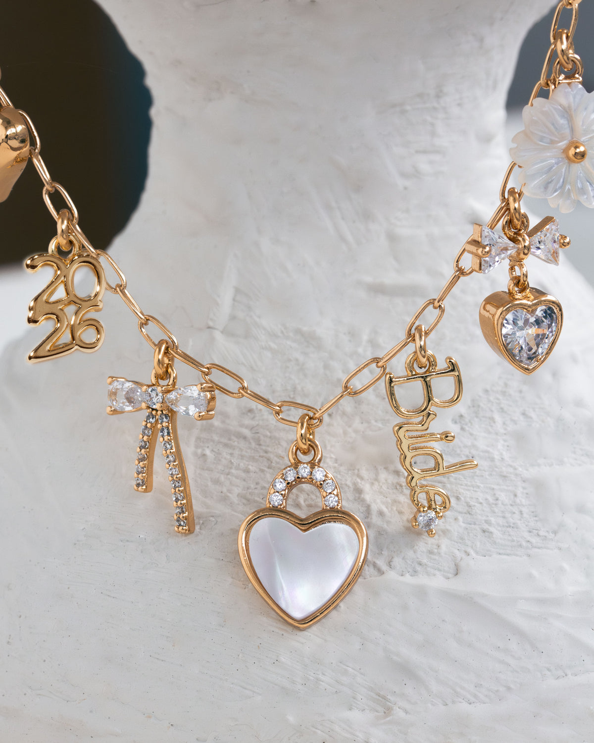 Gold necklace with various charms on a textured white surface