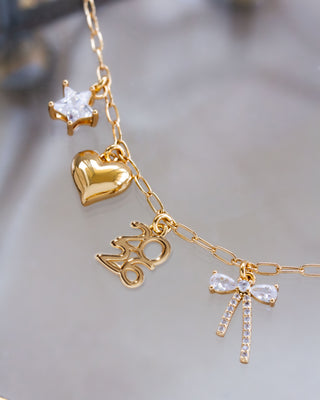 Gold necklace with heart, star, and bow-shaped charms on a blurred background