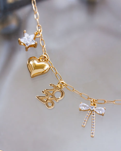 Gold necklace with heart, star, and bow-shaped charms on a blurred background