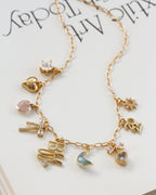 A gold-tone charm necklace  features multiple delicate charms, including a bow, moon, star, and hearts, some embellished with clear rhinestones and pastel-colored stones.