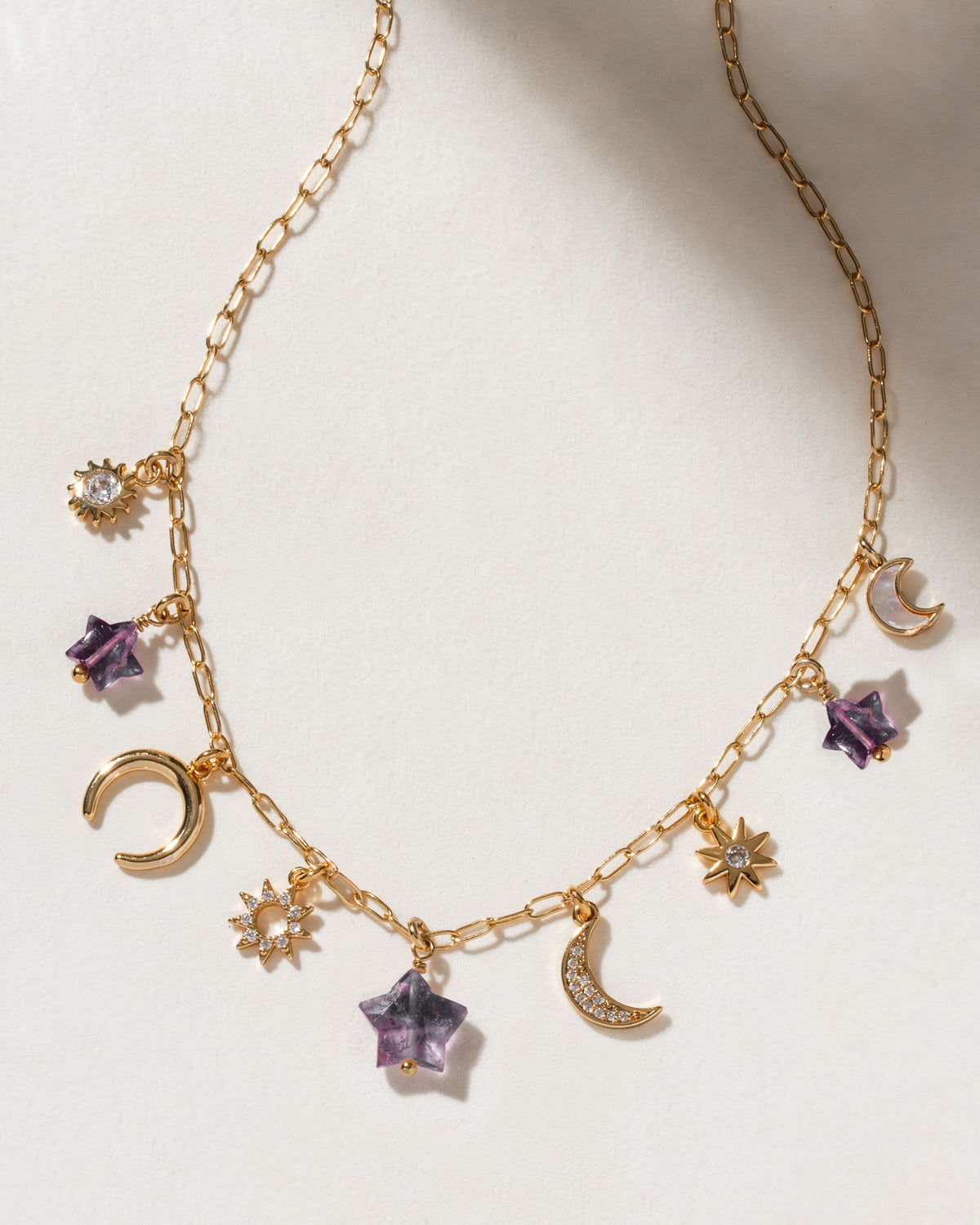 Gold charm necklace with celestial charms, including amethyst star accents.