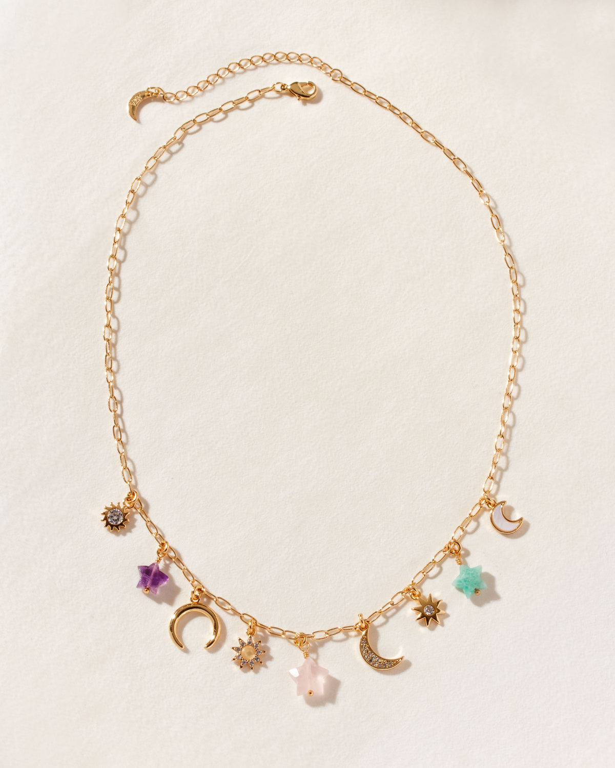 Gold charm necklace with Amethyst, Multistone star, moon, and sun charms on a paperclip chain.