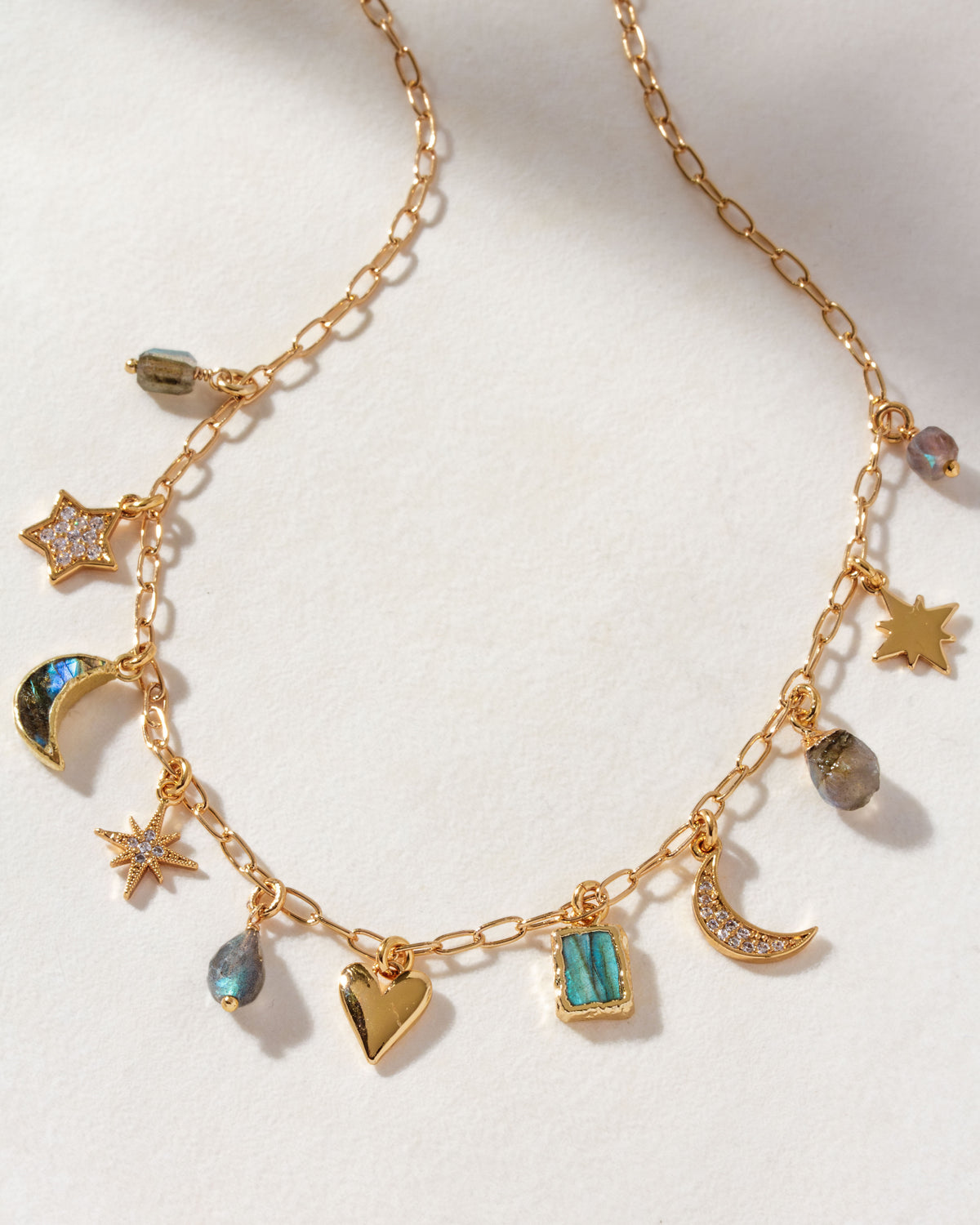 A gold charm necklace with various celestial and heart-shaped charms, with labradorite stones.