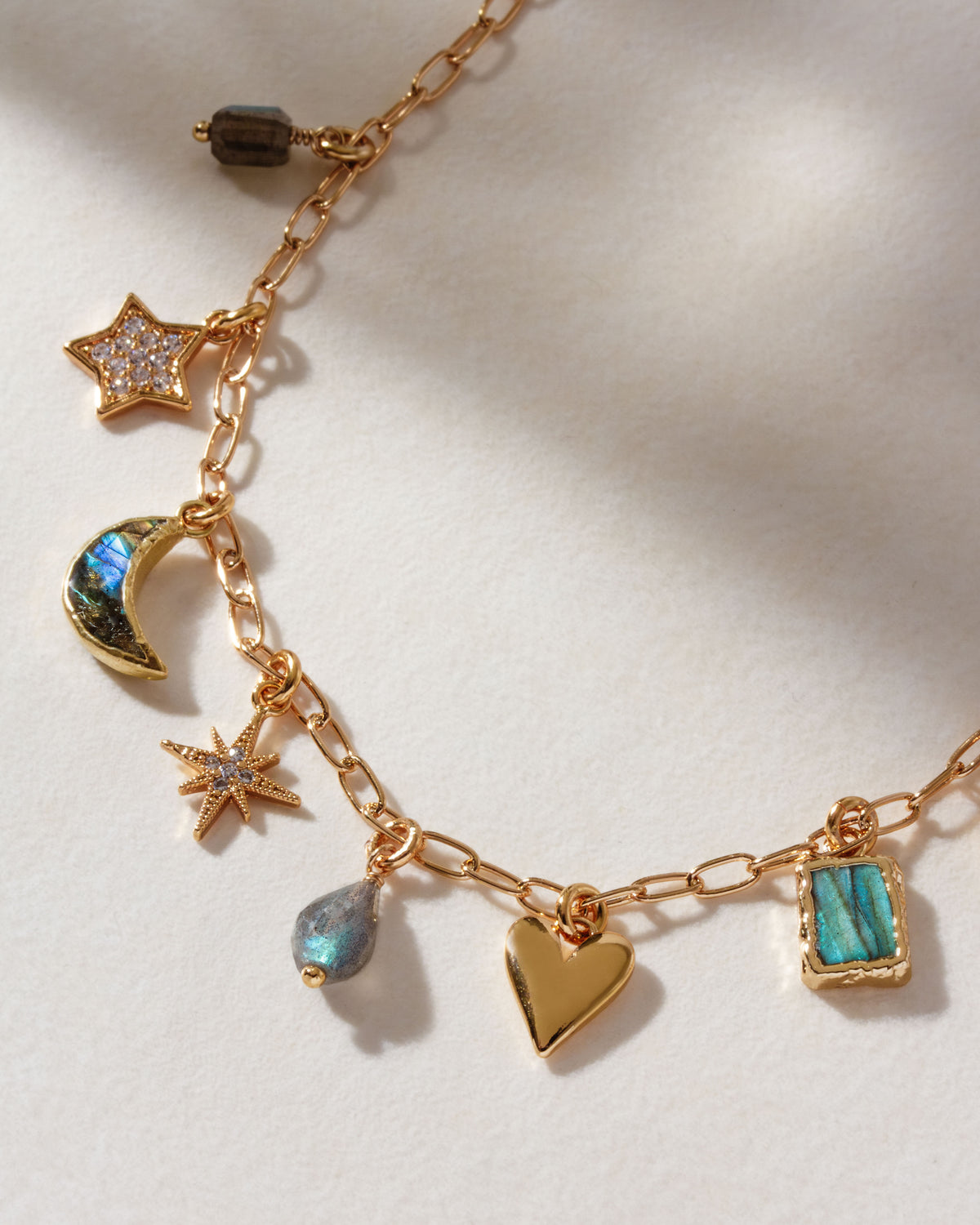 Closeup of gold necklace with many different gold and labradorite charms on a white surface.