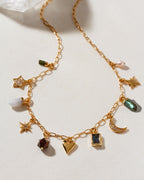 Gold chain necklace with various heart, star, pendant, moon, geometric, and pendant gemstone charms on a light background