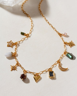 Gold chain necklace with various heart, star, pendant, moon, geometric, and pendant gemstone charms on a light background