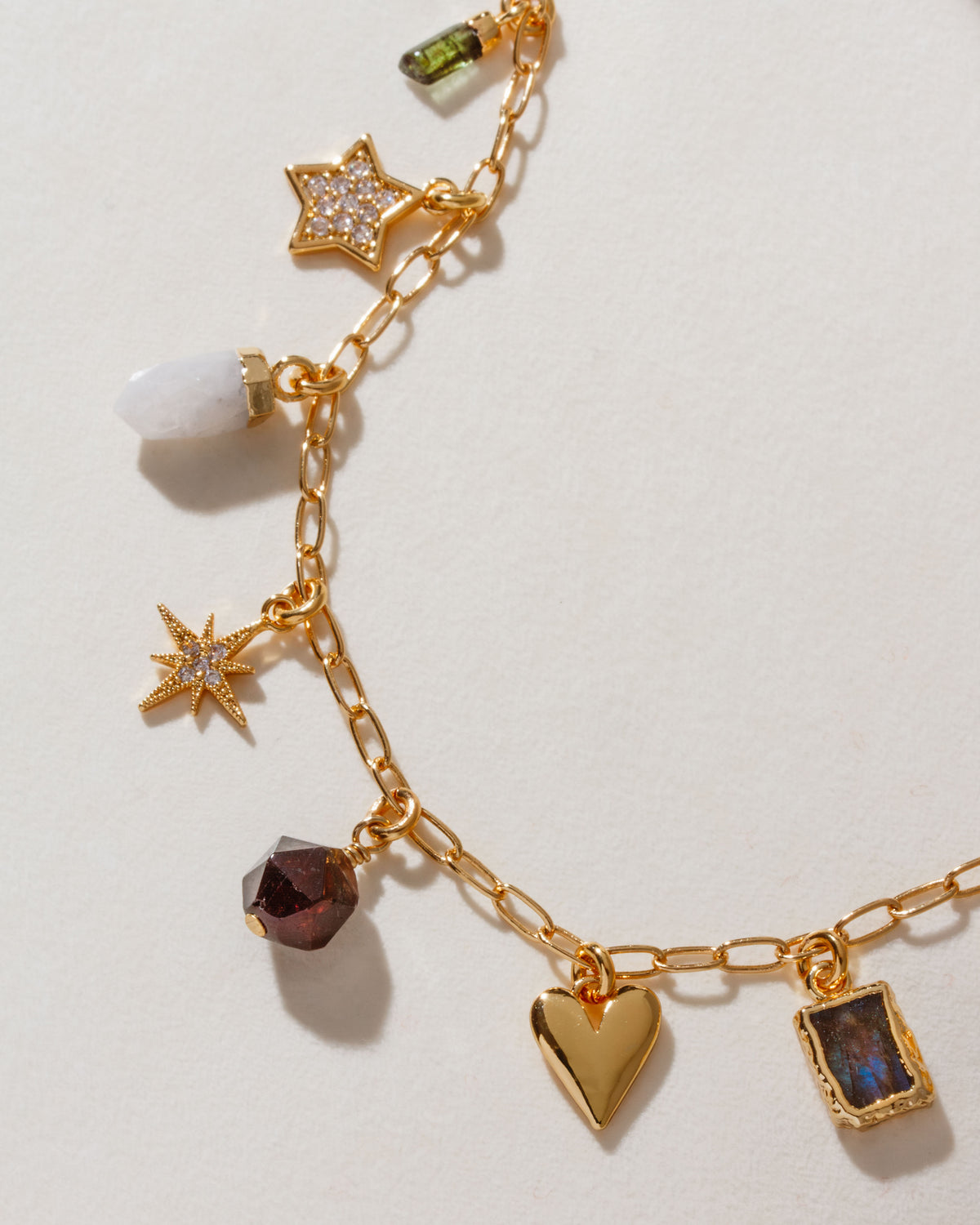 A gold-tone charm necklace with a variety of celestial charms including a moon, beads, and stars on a white surface.