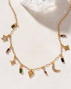A gold-tone charm necklace with a variety of charms including stars, hearts, and moon shapes, as well as different colored beads.